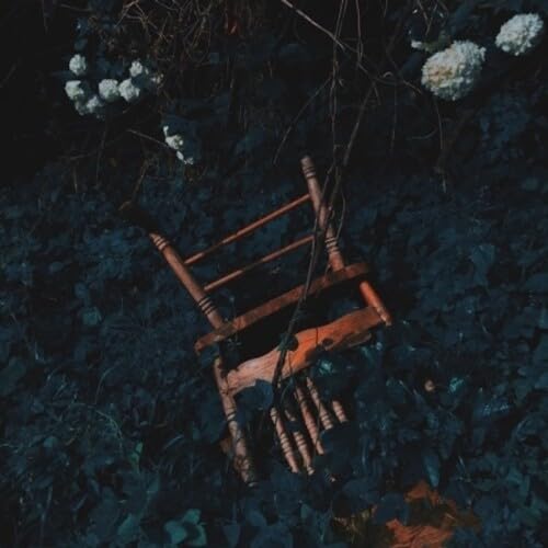 Overturned wooden chair surrounded by dark foliage and white flowers.