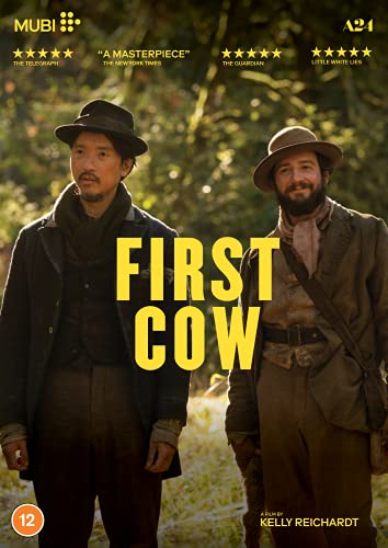 Two men in 19th-century clothing stand in a wooded area; "First Cow" title.
