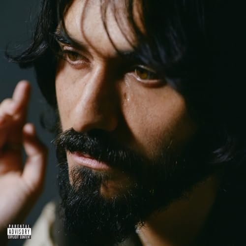 Close-up portrait of a man with dark hair and beard, looking intently.