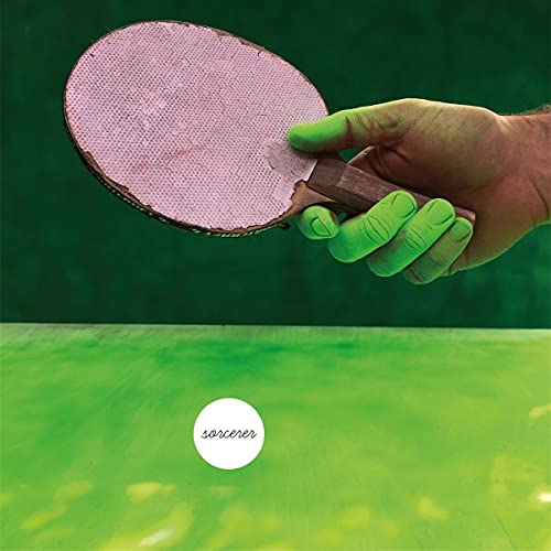 Hand holding a pink ping pong paddle over a green surface.