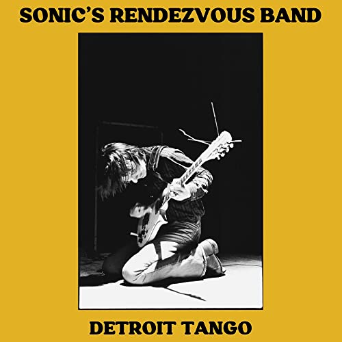 Album cover: guitarist kneeling, playing on a dark stage.