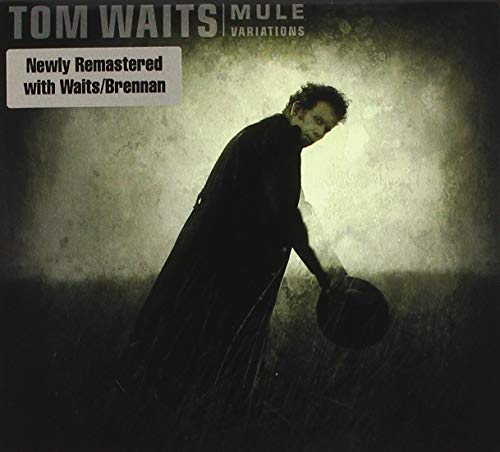 Tom Waits stands in a dark field holding a hat on the album cover.