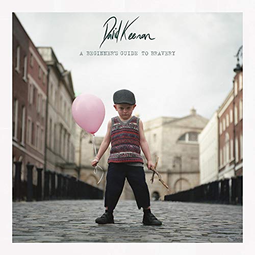 Boy with balloon stands on cobblestone street, album cover art.