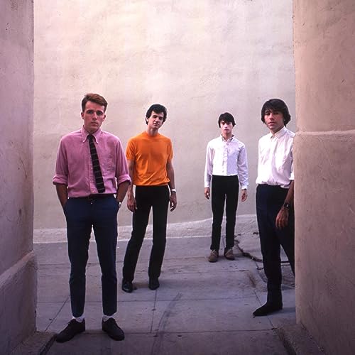 Four men in vintage clothing stand between pale pink walls.