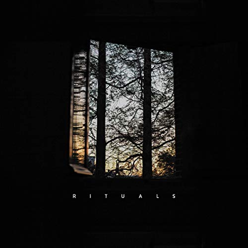 A view of silhouetted trees through a dark window with the word RITUALS below.