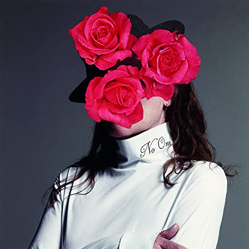 Person in white turtleneck with face obscured by red roses and a hat.