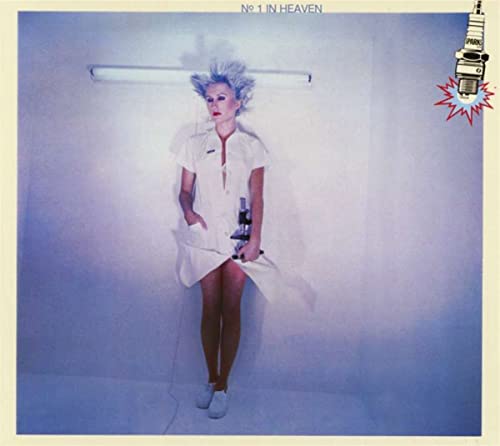 A person with spiky hair in a white uniform stands against a blue wall.