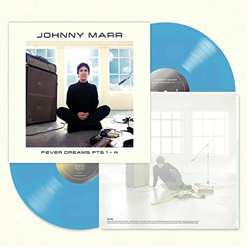 Man sitting cross-legged on floor with blue vinyl records and album cover.