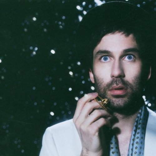 Close-up of Jamie Lidell with wide eyes, holding a small golden object.
