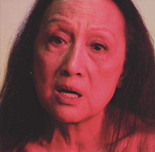Close-up portrait of Anohni with reddish lighting and dark hair.