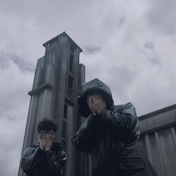 Two people in black hooded jackets covering their faces beforeHB before a tower.
