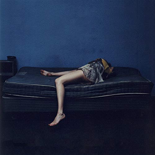 Album cover: person lying on a mattress in a blue room.
