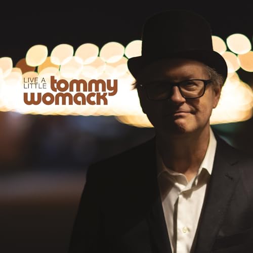 Tommy Womack in a hat and suit, blurred lights in background.