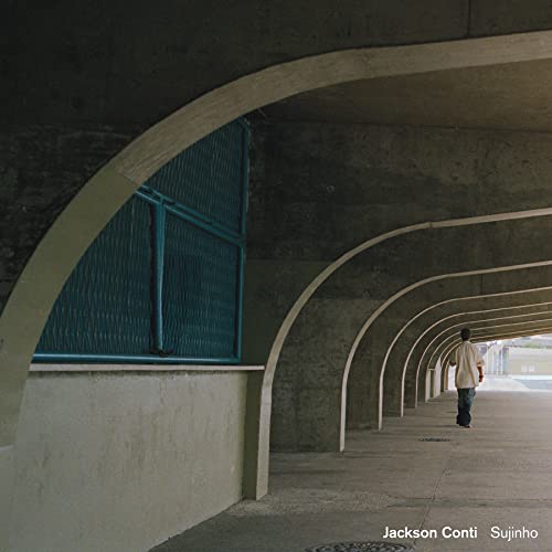 Man walking down an arched concrete corridor, album cover art.