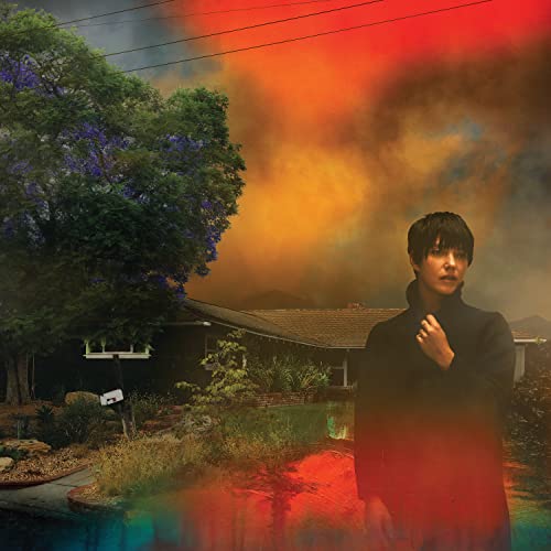Sharon Van Etten stands before a house with a fiery, smoky sky.