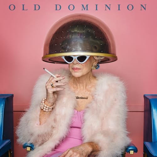 Woman under a hair dryer wearing sunglasses and a pink coat.