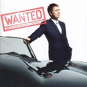 Cliff Richard in a suit leans on a vintage silver car, "WANTED" stamp.