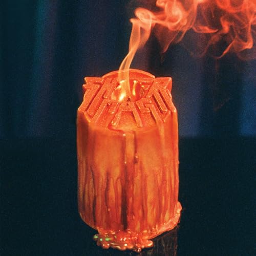 Burning orange candle with the band name "Sheer Mag" embossed on it.