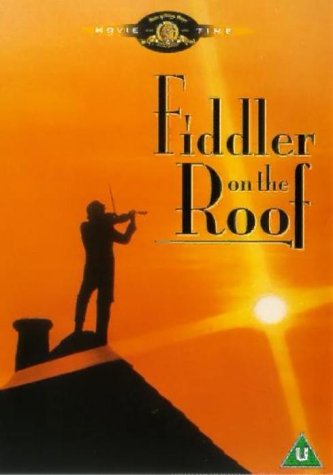 Silhouette of a fiddler on a roof against an orange sunset.