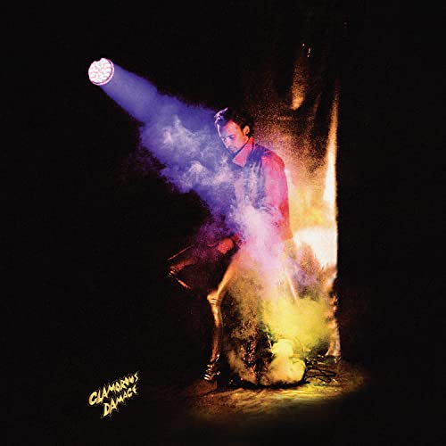 A man stands in a spotlight surrounded by colorful smoke against a black background.