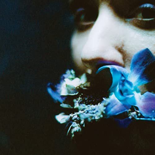 Close-up of a person with blue orchids held to their lips.