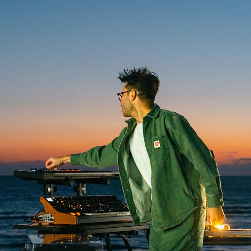Man with glasses operating electronic music equipment at sunset.