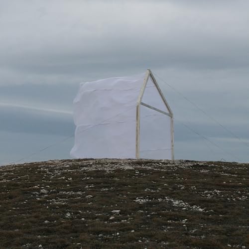 House-shaped sculpture covered in white fabric on a grassy hill.