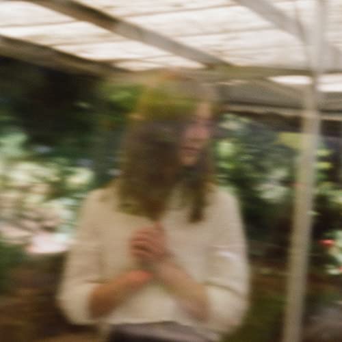 Soft-focus portrait of a woman with long hair, surrounded by greenery.