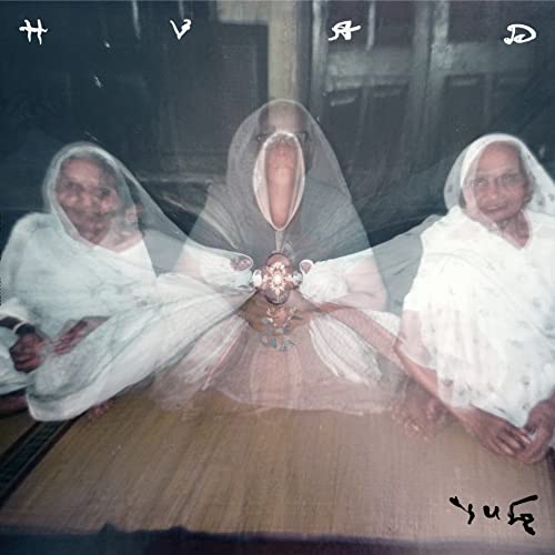 A triple-exposed, ghostly image of three women wearing white headscarves sitting on a mat.