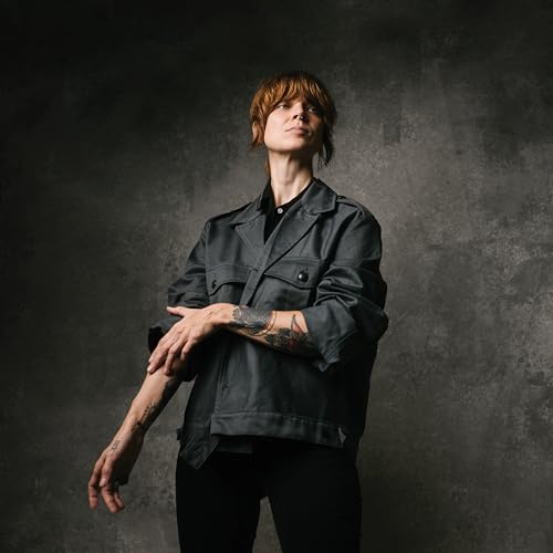 Sarah Shook, with tattoos, looks upward wearing a dark jacket.
