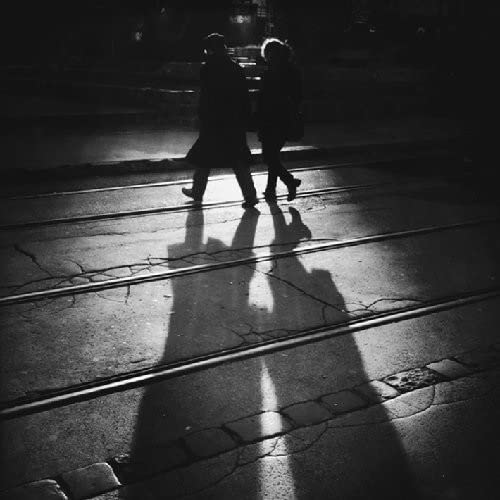 Black and white photo of three figures walking on a wet street.
