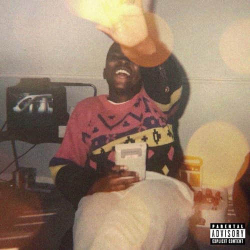 Man in colorful sweater, holding a cassette tape, blurry background.