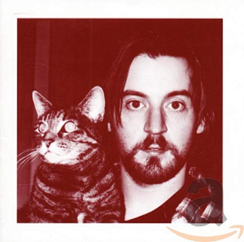 Red-tinted photo of a bearded man standing next to a tabby cat.