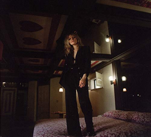 Woman in a black suit standing on a patterned bed.