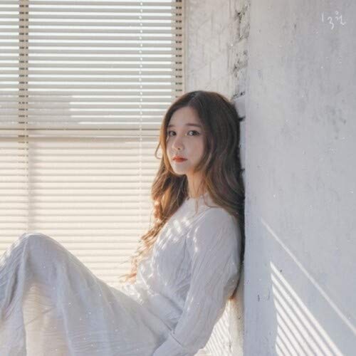 Woman in white dress posing near a window with blinds.