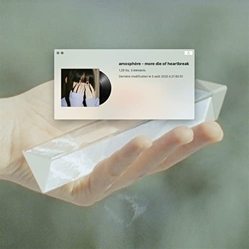 Hand holding a translucent block with a computer screen displaying album art.