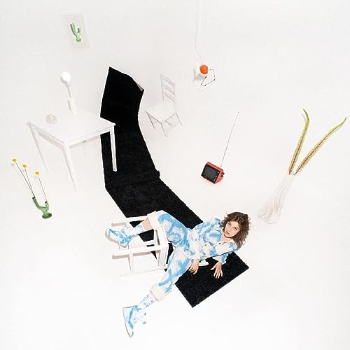 Person in patterned clothing lying among furniture and objects.