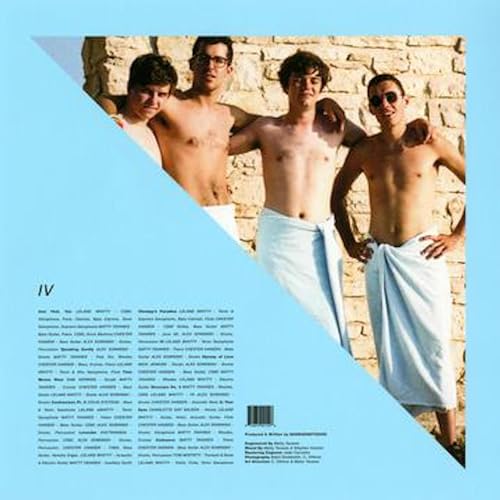 Four shirtless men with towels pose against a stone wall.