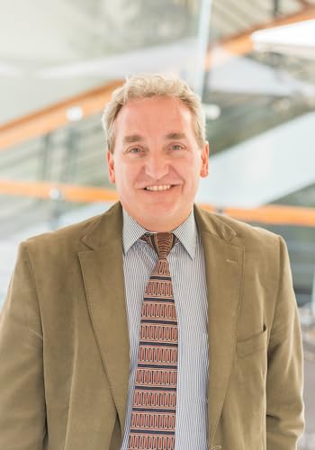 Man in suit and tie smiles, book cover blurred in background.