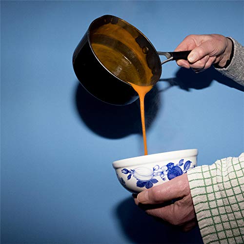Hands pouring orange liquid from a black pot into a blue-patterned white bowl.