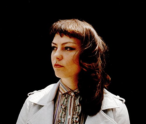 Angel Olsen portrait, looking left, wearing a striped shirt and jacket.
