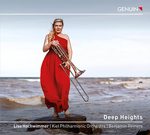 Woman in red dress holding a trombone on a beach.
