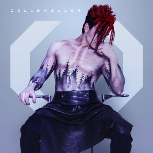Shirtless man with red-streaked hair and chest tattoos sitting against a light background.