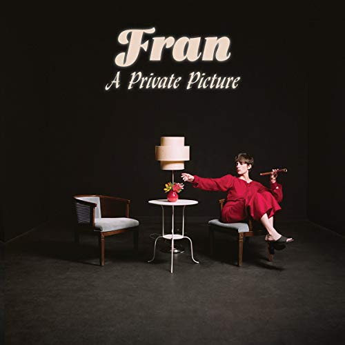 Woman in red robe seated in a minimalist, dark room.