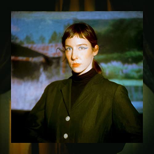 Portrait of a woman with blue eyeliner wearing a dark blazer and turtleneck.