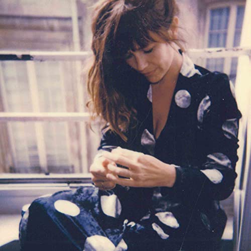 Woman with long hair in patterned clothing, looking down at hands.