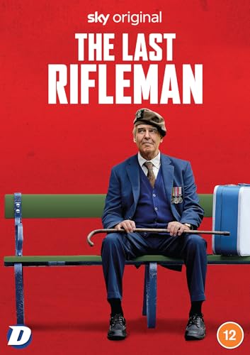 An elderly veteran in a suit and beret sits on a bench against red.