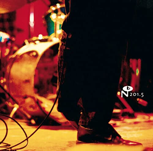 A person's legs and feet stand on a stage with a drum set behind them.