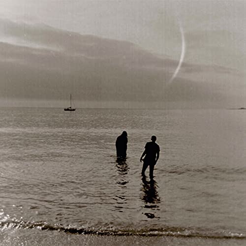 Two figures stand in shallow water under a hazy sky.