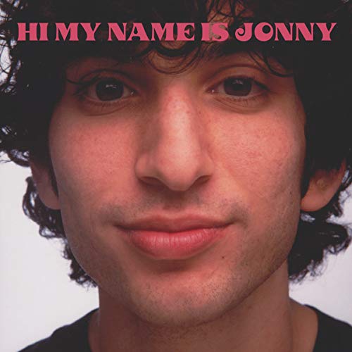 Close-up portrait of a young man with curly dark hair, pink text overlay.